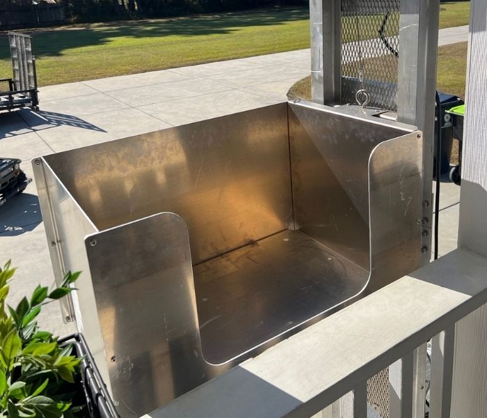 Metallic outdoor platform lift for home elevators by a porch, overlooking a paved area and lawn.
