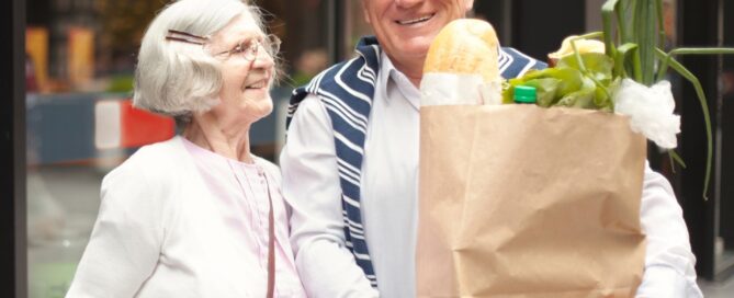 Smiling older couple holding a grocery bag, enjoying a day out together.