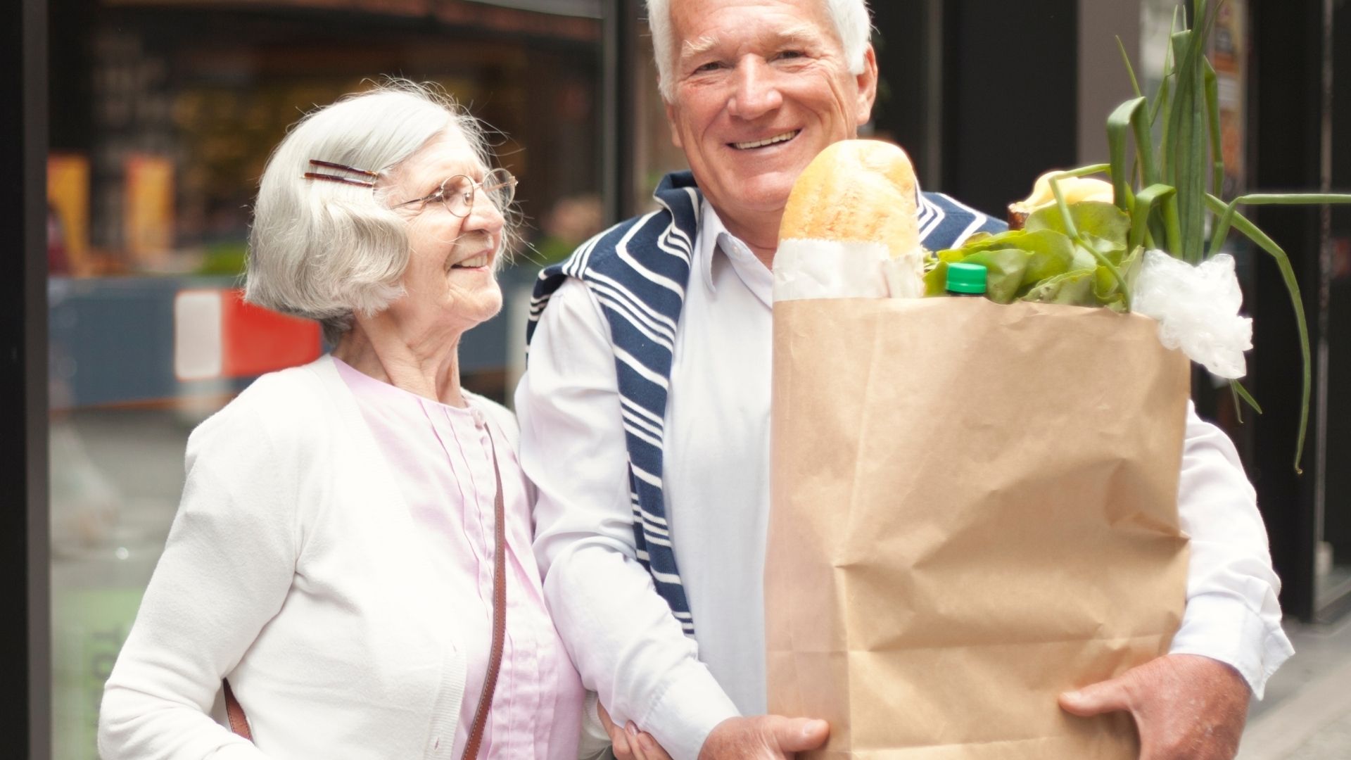 Smiling older couple holding a grocery bag, enjoying a day out together.