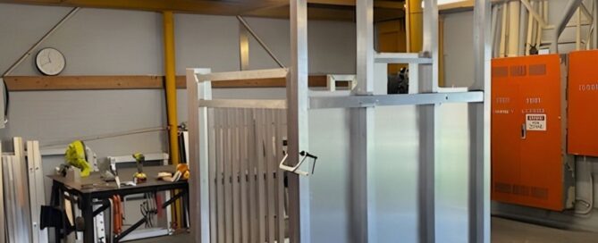 Home elevator frame in a workshop with tools and orange panels in the background.