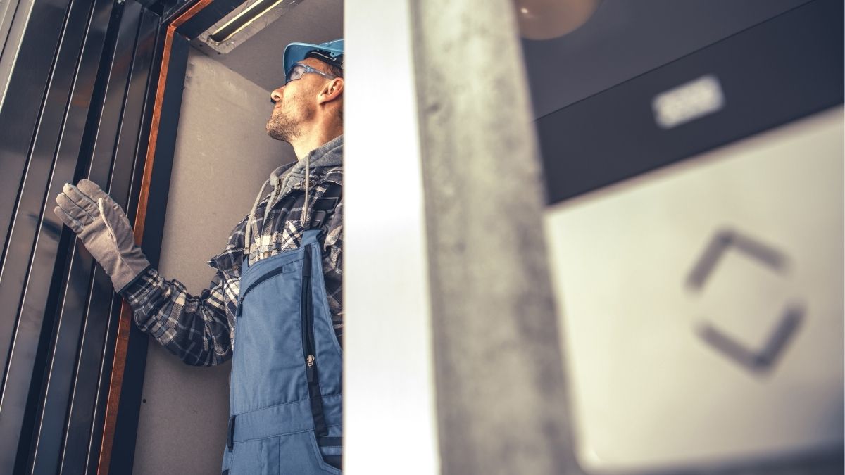 Man Maintenancing Elevator Technician in overalls and safety gear inspecting home elevator shaft, focusing on door mechanisms.