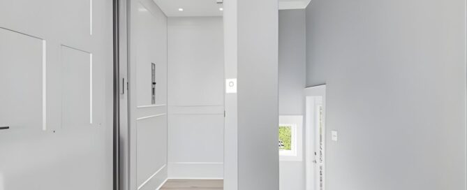 Modern gray home elevator with open doors, adjacent to a staircase. Brightly lit interior and sleek design.