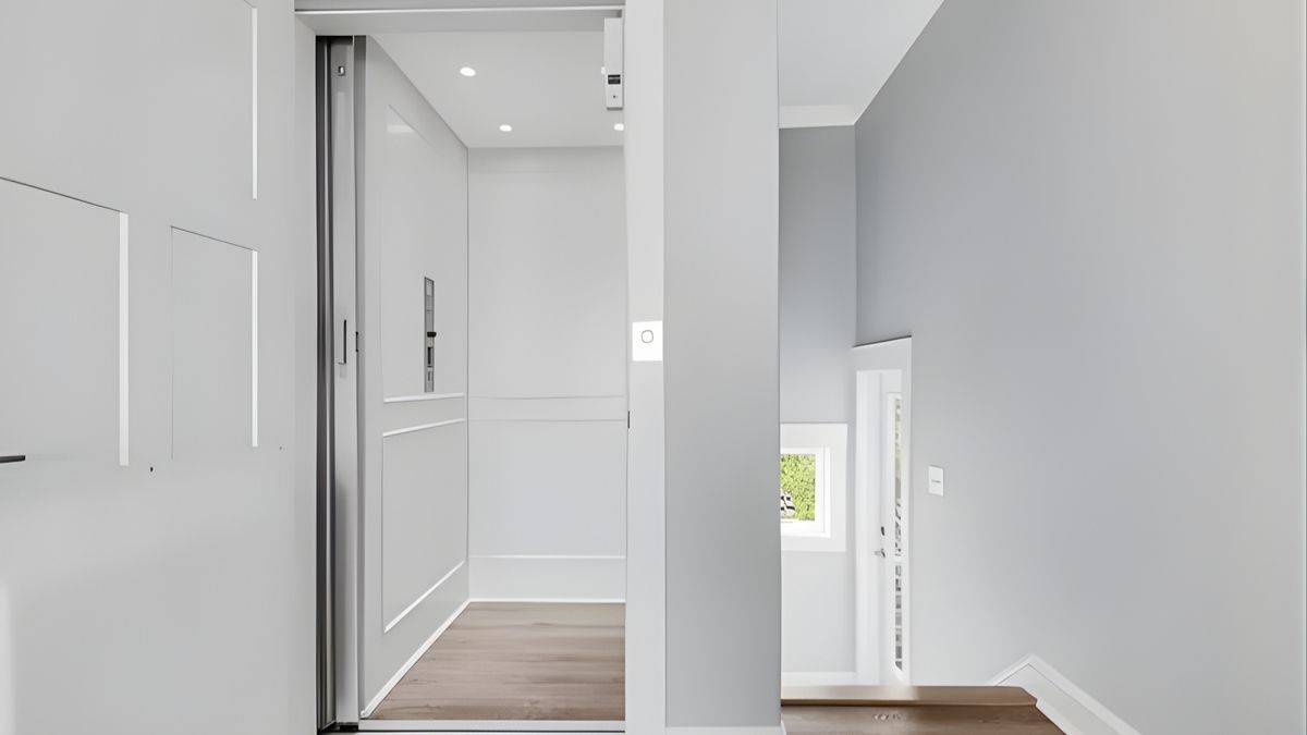 Building a Coastal Home When to Start Planning for a Home Elevator Modern gray home elevator with open doors, adjacent to a staircase. Brightly lit interior and sleek design.